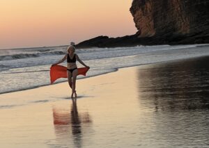 Charla Hathaway with red scarf on a beach at sunset representing power and freedom for women