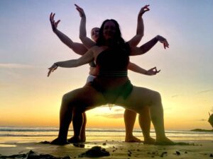 Playful people in goddess pose at sunset on a beach.